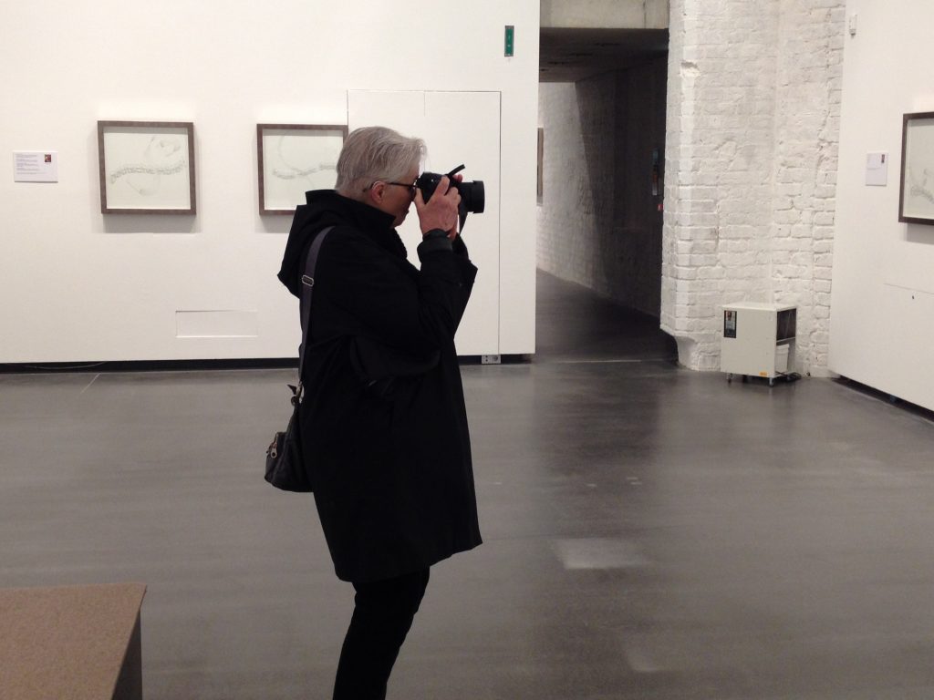 Image of Linn Underhill standing in a gallery with a camera to her eye